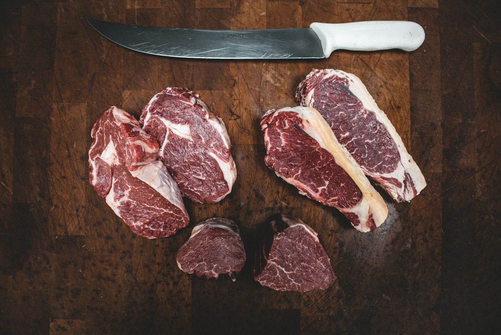 Selection of premium beef cuts neatly arranged on a wooden butcher block beside a clean butcher knife