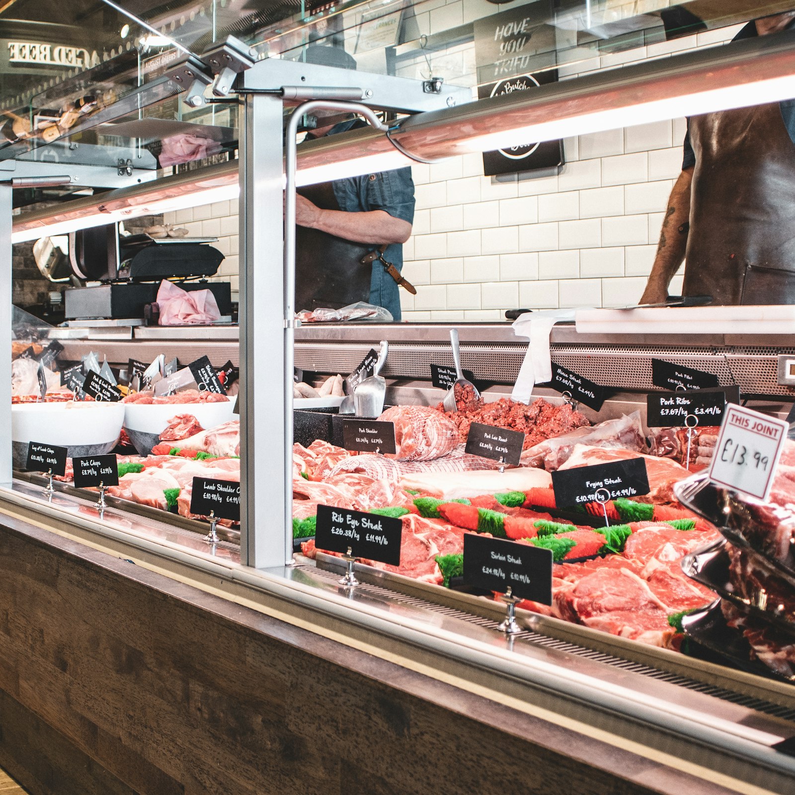 Bright modern butcher shop counter with neatly arranged fresh cuts and staff serving customers in the background
