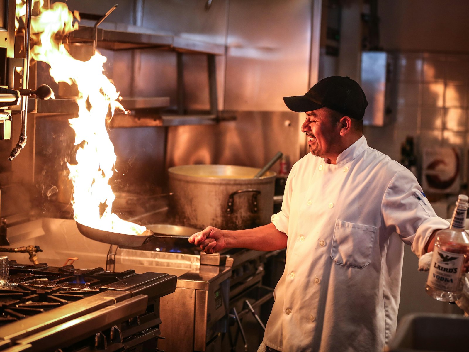 Smiling chef tossing a flaming wok on the line of a busy restaurant kitchen