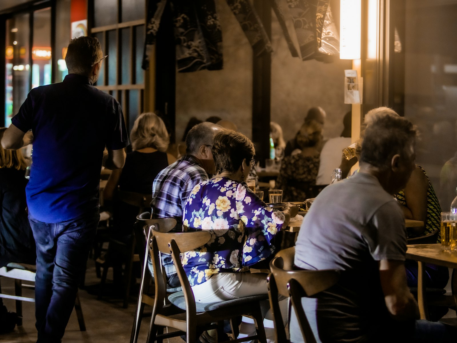 Full restaurant at night with every table occupied and a waiter heading to the kitchen