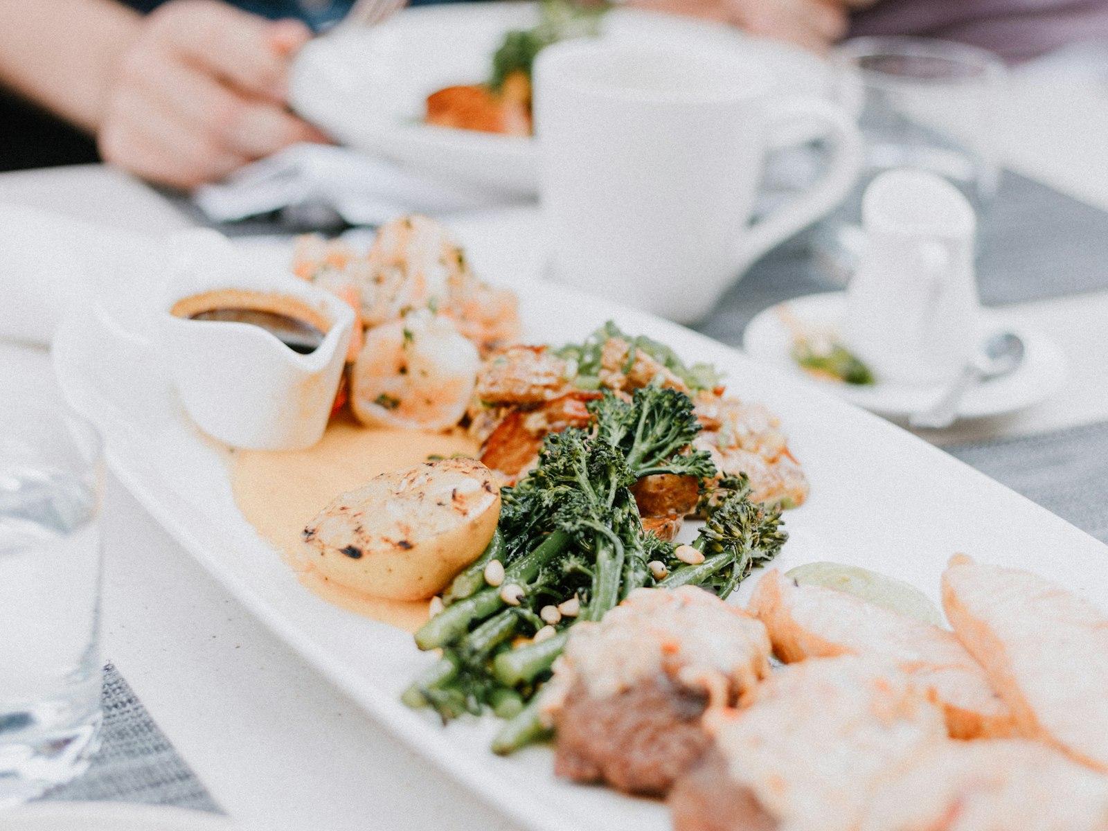 Friends sharing a plate of seafood and grilled vegetables across a restaurant table