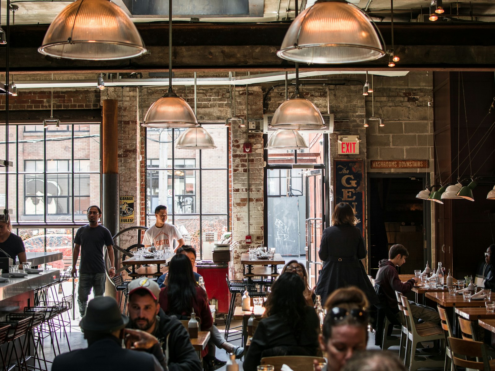 Packed indie restaurant with exposed brick walls and copper pendant lights, full of diners and staff